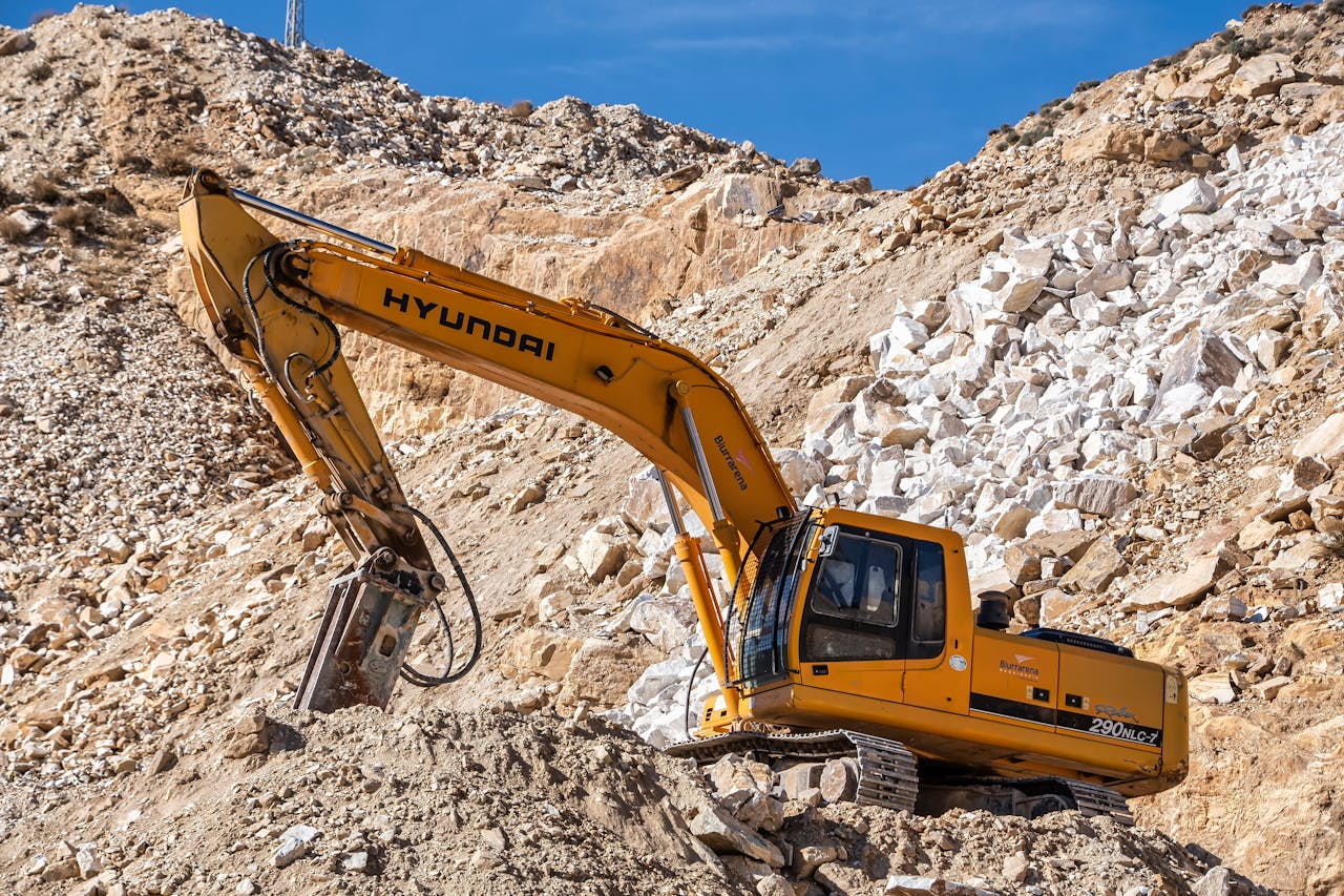 who-we-are Yellow Hyundai excavator operating in a rocky quarry under a clear blue sky. Perfect for industrial themes.