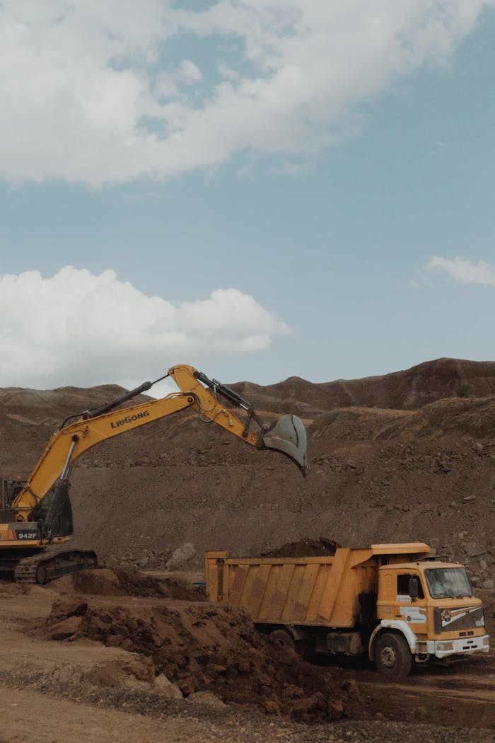about-us Yellow excavator and dump truck operating in a mining setting under a blue sky.